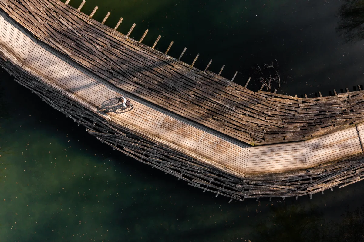 Eine aus Holz gebaute Brücke, ein Velofahrer fährt drüber.